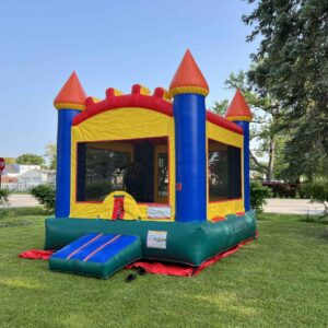 Colorful arch-style bounce house with red, yellow, blue, and green castle towers set up on a grassy lawn in a neighborhood.