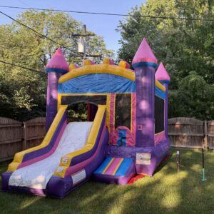 Pink and purple combo bounce house with an attached slide set up on a grassy backyard lawn.
