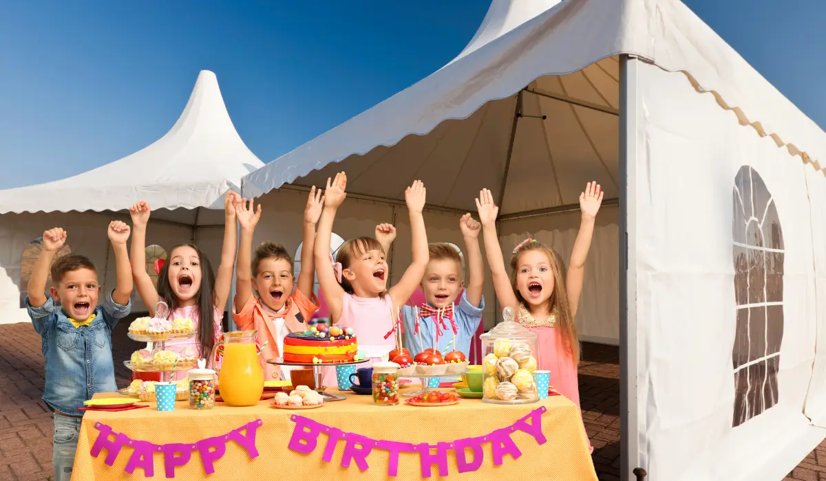 Children celebrating Fall Birthdays under large white party tents with colorful decorations, desserts, and joyful expressions at an outdoor event.