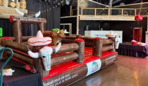 Indoor mechanical bull rentals setup with inflatable padding for corporate kickoff team building entertainment events.