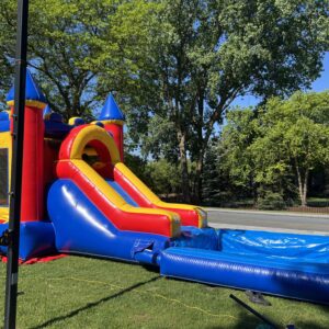Colorful inflatable wet combo bouncer with a slide and splash pool set up on a grassy lawn on a sunny day.